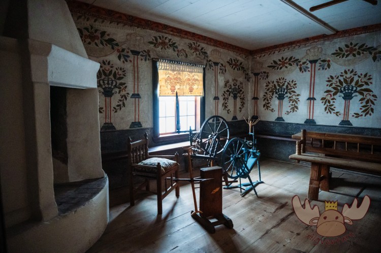 Ein Wohnraum in einem rekonstruierten Gebäude im Freilichtmuseum Skansen mit Heizstelle, bemalten Wänden und Möbeln aus vergangenen Zeiten. | A living room in a reconstructed building at Skansen Open-Air Museum with a heating point, painted walls and furniture from times gone by.